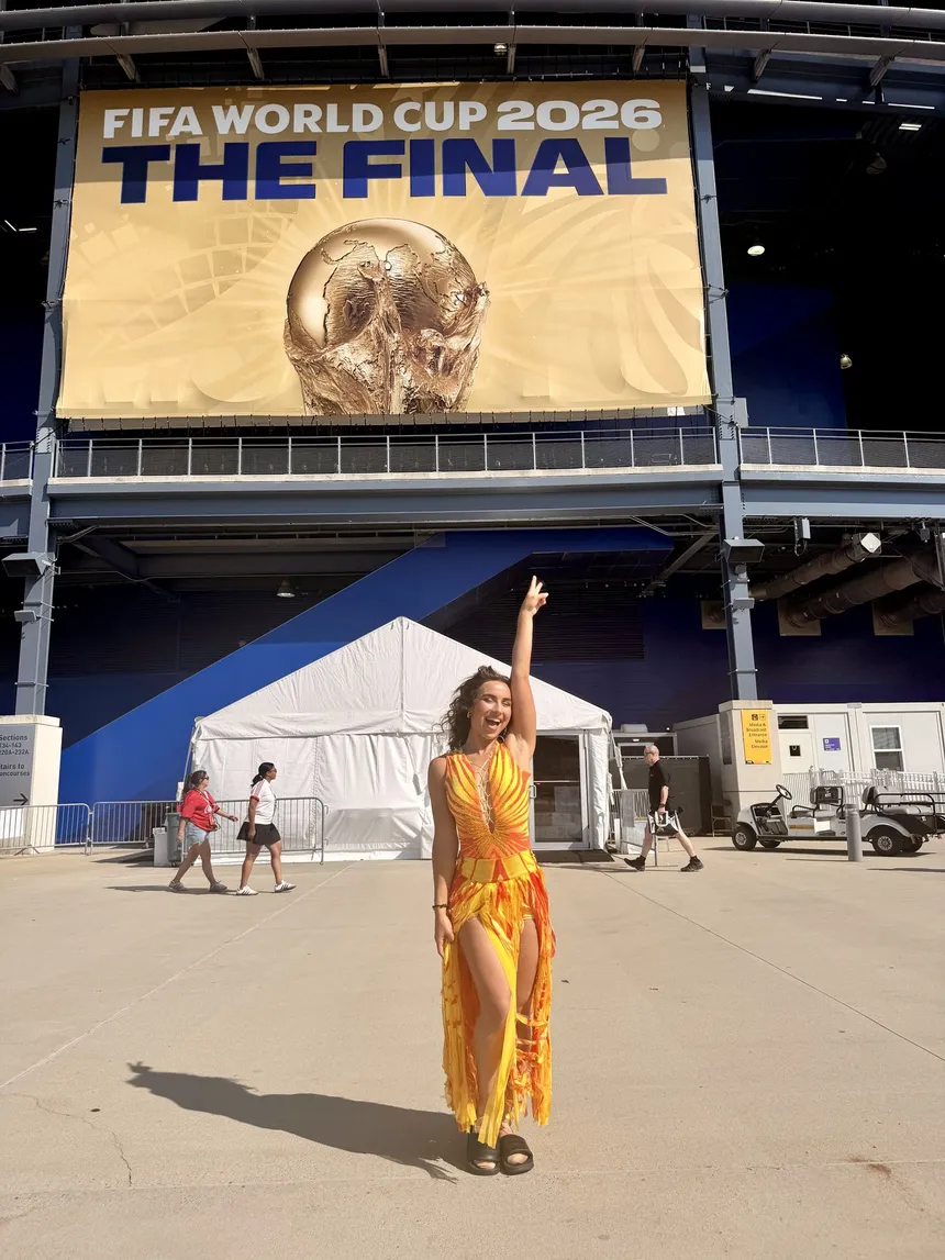 Enola Bedard in a yellow-and-orange performance dress beneath the FIFA World Cup 2026 'The Final' banner at the stadium.